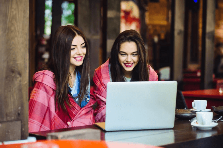 two-young-beautiful-girl-sitting-table-looking-something-internet